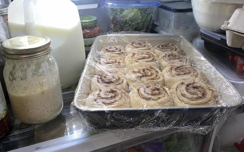 Pan of shaped cinnamon rolls covered in plastic wrap chilling overnight in the fridge